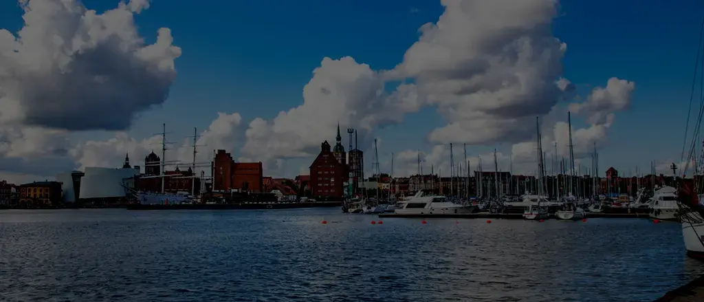 Blick über das Wasser auf den Stralsunder Hafen mit Segelmasten und Backsteinbauten
